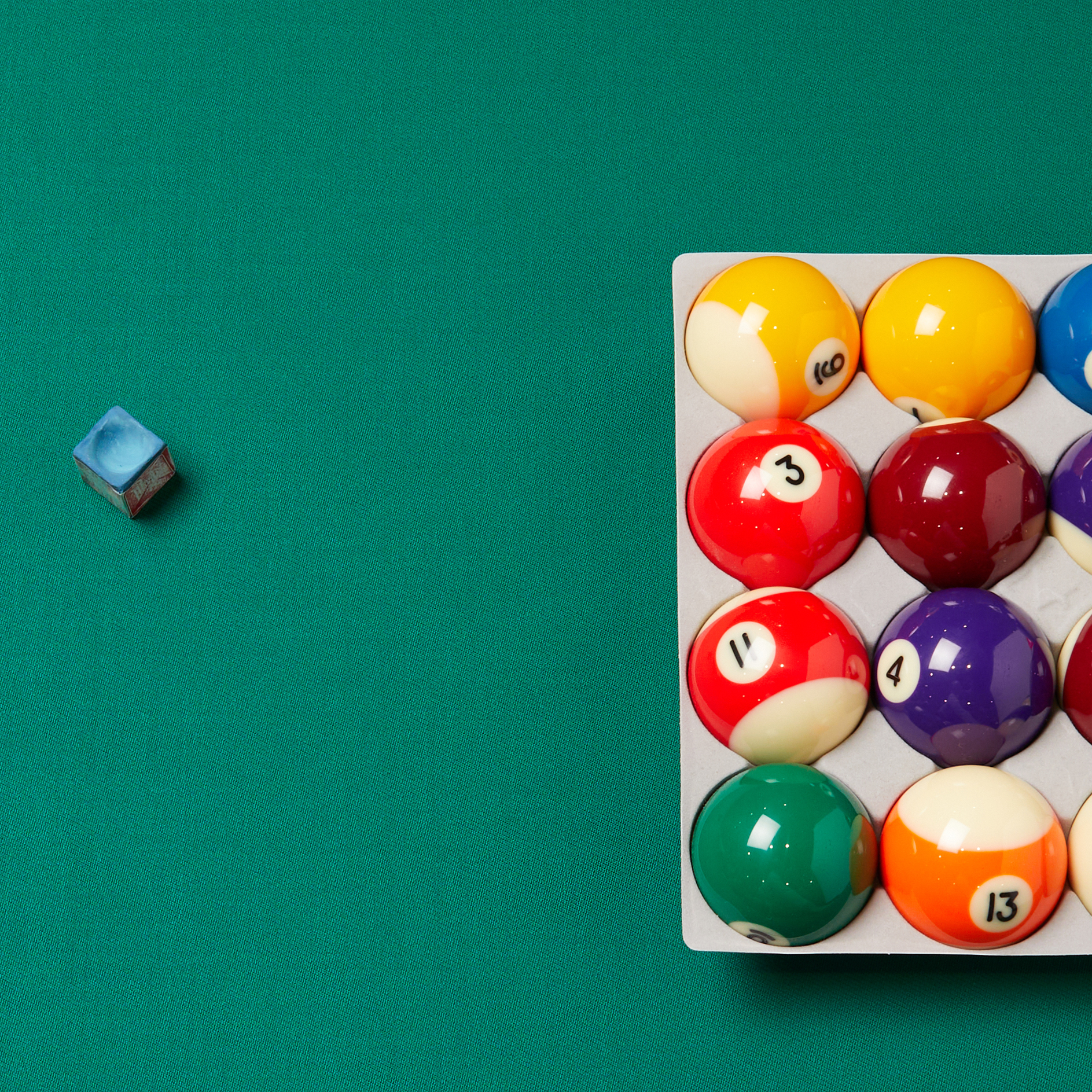 Pool balls in a rack on a green snooker cloth with a chalk cube beside them, ready for a game of billiards