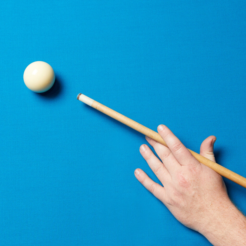 A hand aiming a pool cue at the white ball on a blue snooker table, ready to take a shot.