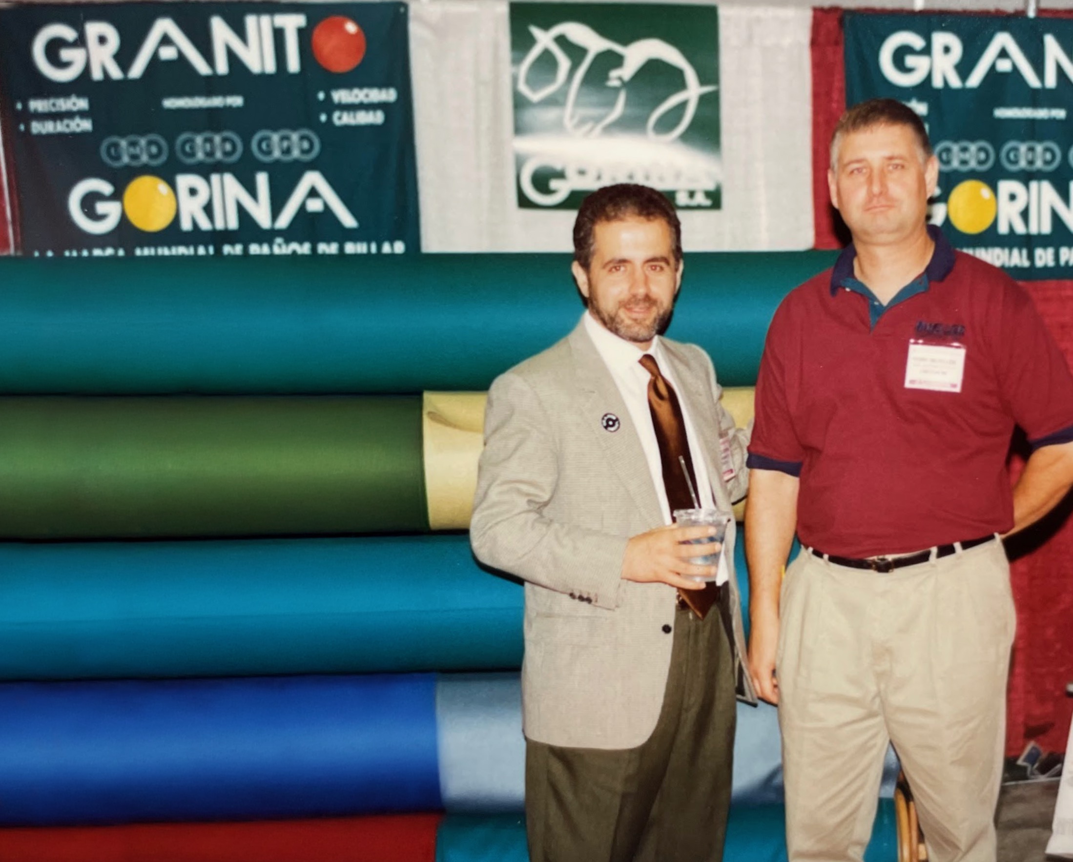 Carlos Gorina and Rory Mueller at a trade event, showcasing Gorina's premium billiard cloths in various colors, highlighting their longstanding partnership